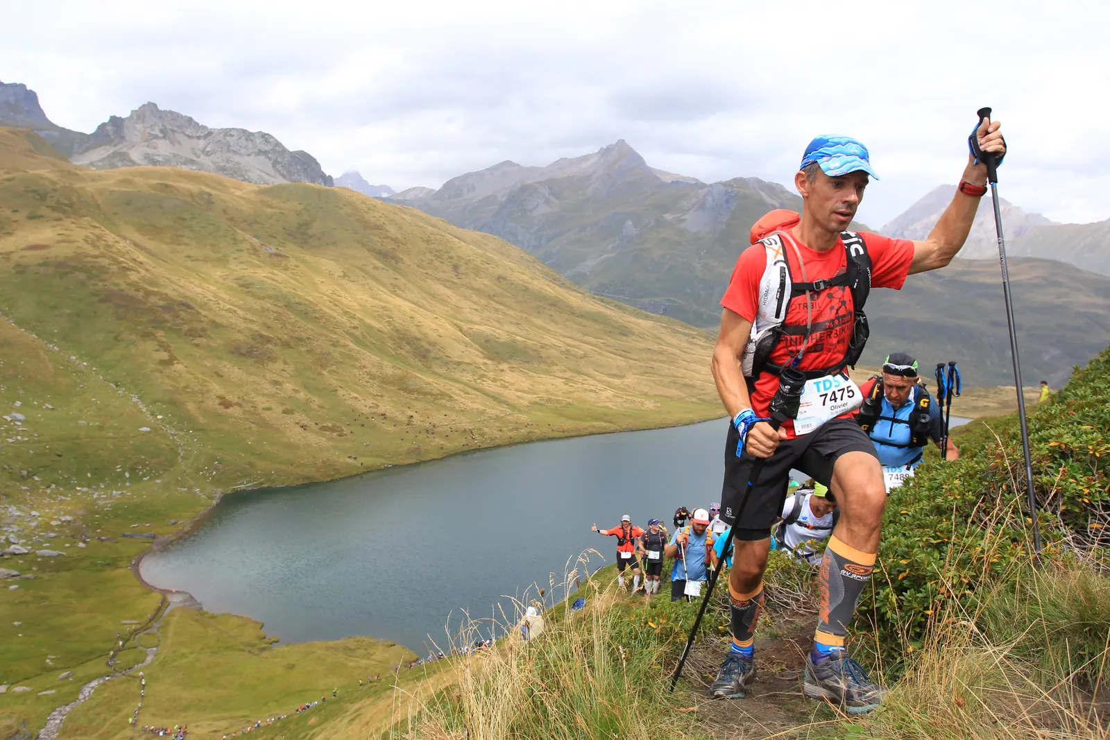 Coureur en tenue rouge en montée sur le sentier au-dessus d’un lac de montagne.
